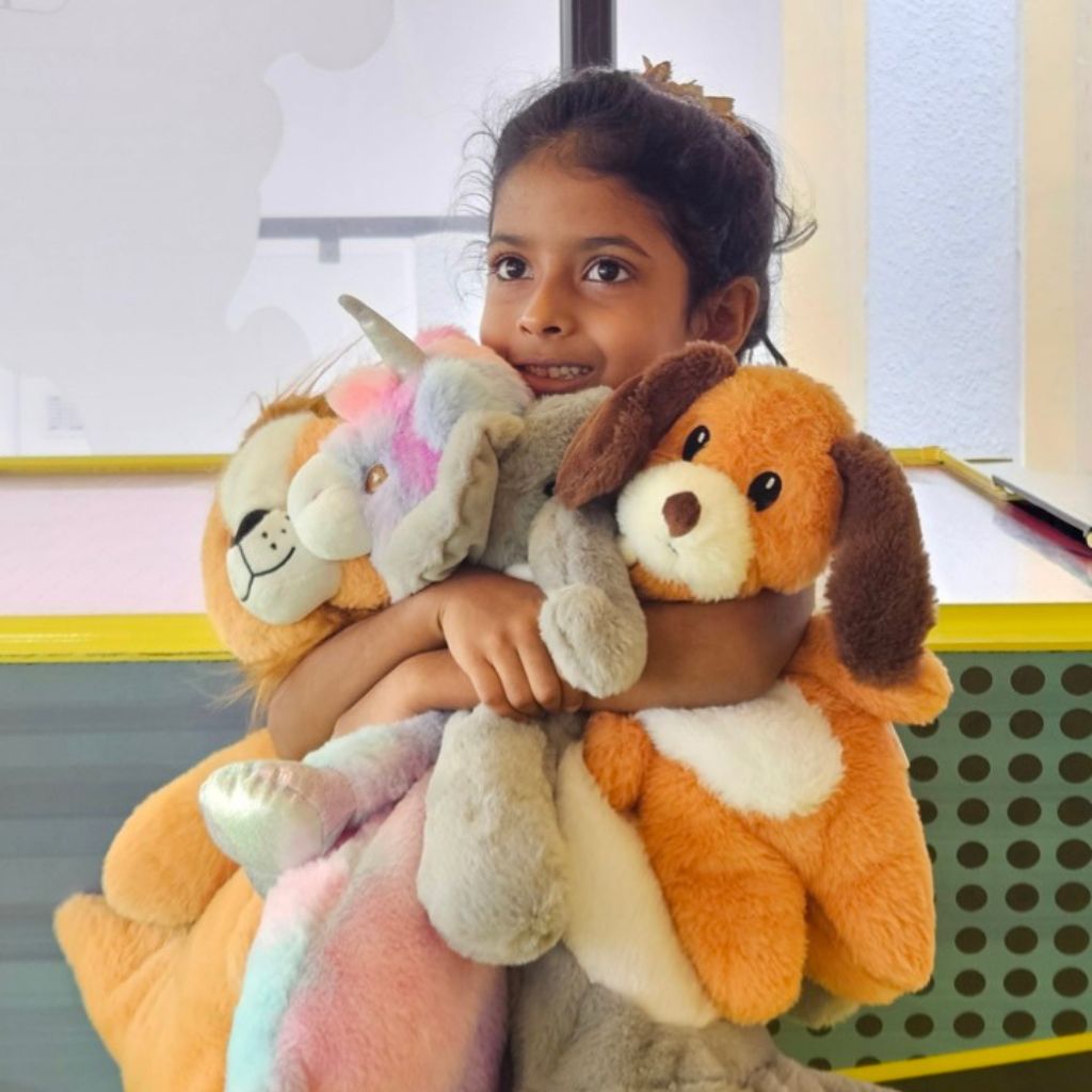 Child holding multiple stuffed animals in a classroom setting