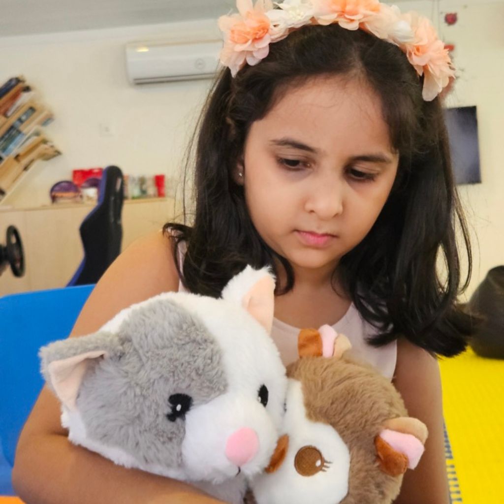 Young girl holding two plush toys in a classroom setting