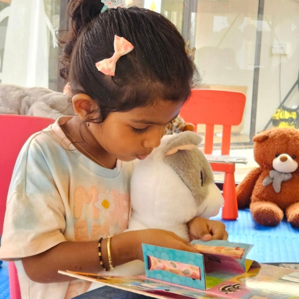 Child reading a book with stuffed animals around in a casual setting