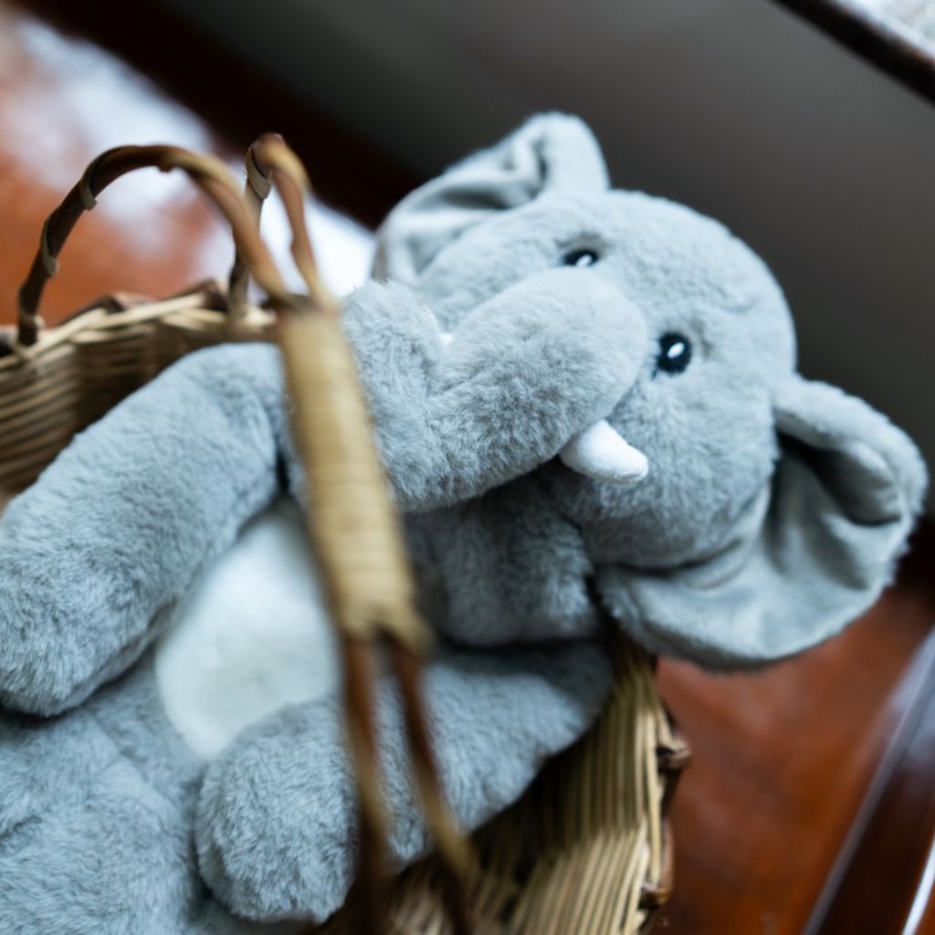 Gray plush elephant toy in a wicker basket on a wooden surface