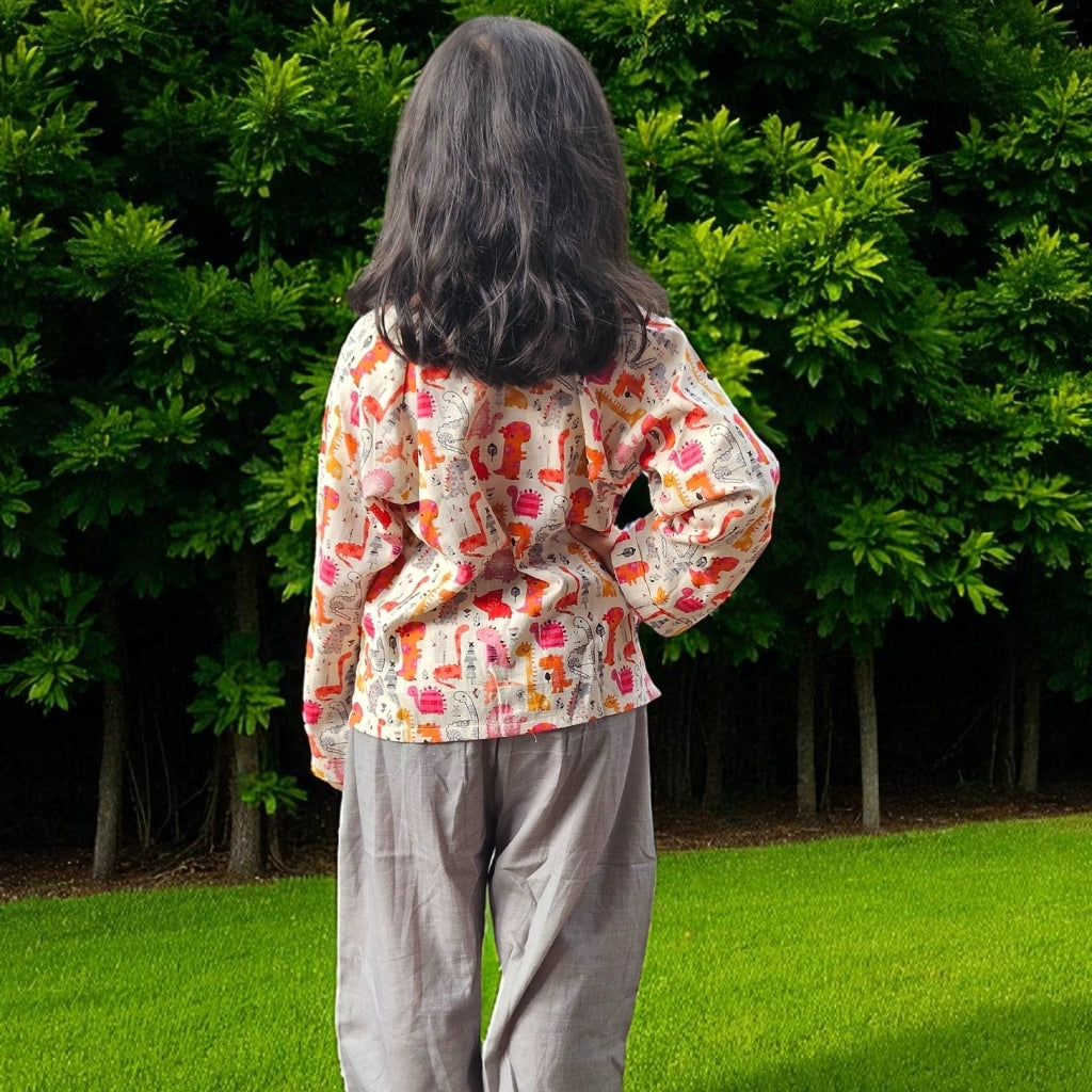 Person wearing a colorful patterned shirt and gray pants standing in a grassy area with green bushes.