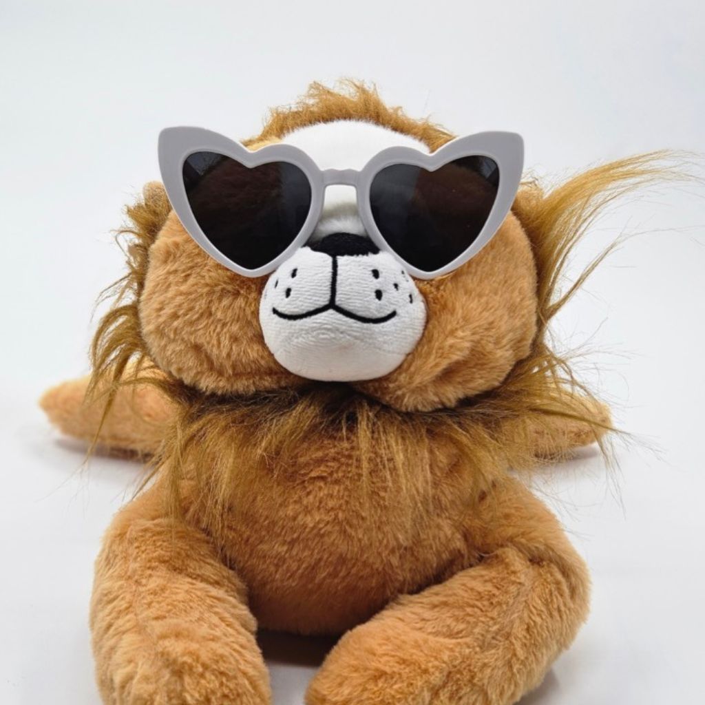 Plush lion toy wearing heart-shaped sunglasses on a white background
