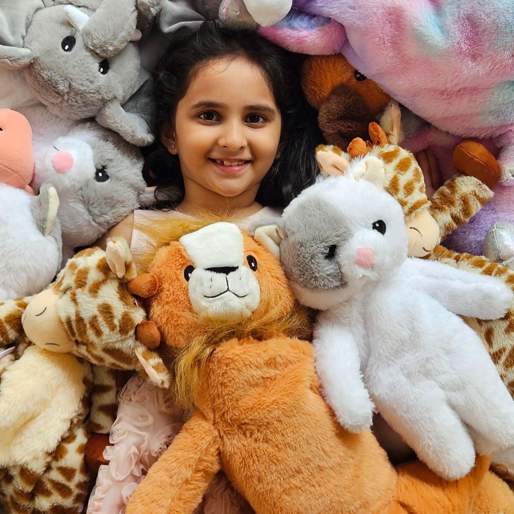 Child cuddling SnuggyBuggy plush toys — lion, giraffe, elephant, and other soft stuffed animals.