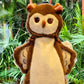 Plush toy owl with brown and beige colors against a green leafy background
