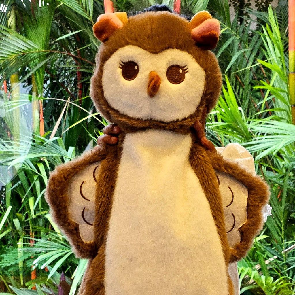 Plush toy owl with brown and beige colors against a green leafy background