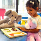 Child playing with SnuggyBuggy plush toys — pastel unicorn and grey elephant — while reading a picture book